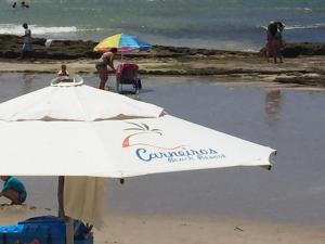 een witte parasol op het strand met mensen in het water bij Carneiros Resort Beira Mar Térreo in Praia dos Carneiros