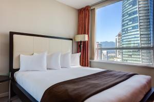 a bedroom with a large bed and a large window at Carmana Hotel & Suites in Vancouver