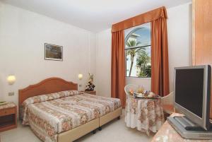 a bedroom with a bed and a tv and a window at Hotel Piccolo Lido in Bordighera