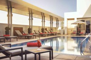 einen Hotelpool mit Liegestühlen, einem Tisch und einem Tisch in der Unterkunft Centro Waha by Rotana in Riad