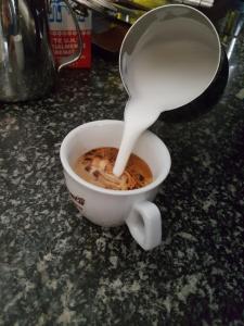 une personne versant du lait dans une tasse de café dans l'établissement Nuovo Hotel Vigevano, à Vigevano