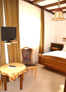 a bedroom with a bed and a chair and a tv at Hotel Wiesengrund in Lindenfels