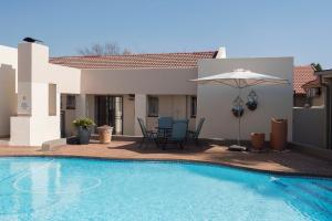 a swimming pool with an umbrella and a house at President Lodge in Edenvale