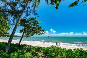 uma praia com pessoas andando na areia e no oceano em Temple 121 Modern Spacious Palm Cove 2 Brm 2 Bth Resort Apartment With Courtyard em Palm Cove