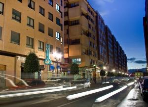 una calle de la ciudad por la noche con coches y edificios en Hotel Playa Poniente, en Gijón