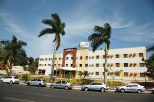 een hotel met auto's voor het hotel met palmbomen bij Villalba Hotel in Uberlândia