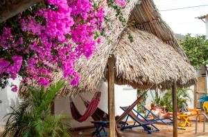 a group of people laying in chairs under a straw umbrella and flowers at Divanga Hostel in Taganga