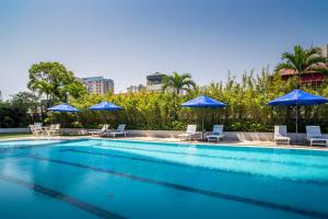 a swimming pool with blue umbrellas and chairs at Rose Garden Residences in Hanoi
