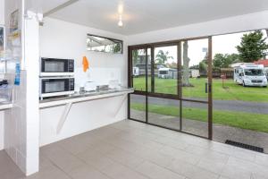 cocina con paredes y ventanas blancas y vistas a un parque en Harbourside Holiday Park, en Whitianga