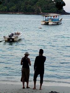 two people standing on the beach with a boat in the water at Iboih inn in Sabang