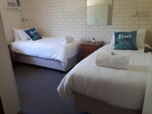 two beds in a room with white sheets and blue pillows at Villa Seven in Kalbarri