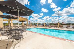 a pool with tables and chairs and a table with an umbrella at Ramada by Wyndham College Station in College Station