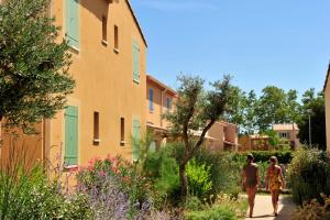 two women walking down a sidewalk in front of a building at Résidence Goélia Le Mas des Arènes in Mouriès