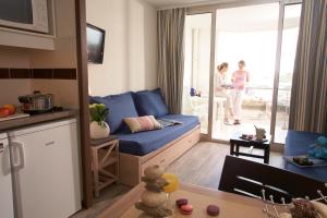 a living room with a blue couch and a woman standing outside at SOWELL RESIDENCES Le Port in Trouville-sur-Mer