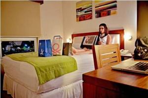 Hotel Hex Estelí في إستيلي: امرأة جالسة على سرير في غرفة فندق