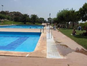 una piscina en un parque con gente sentada en el césped en Apartamentos Rurales San Juan en Castellnovo