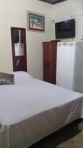a bedroom with a white bed and a refrigerator at Apartamentos no centro in Arraial do Cabo