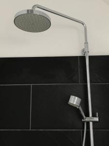 La salle de bains est pourvue d'une pomme de douche et de carrelage noir. dans l'établissement Ferienwohnung Landart, à Hilter