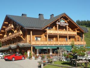 un grand bâtiment en bois avec une voiture rouge garée devant dans l'établissement Hôtel Restaurant "Les Sapins" Wellness & Gourmet, à Manigod