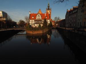 a building with a clock tower next to a river at Grand Tourist Gemini in Gdańsk