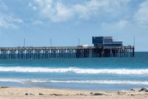 a pier in the ocean with a beach and waves at Sunset Inn in Costa Mesa