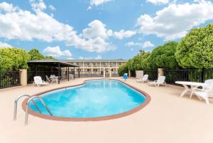 una piscina con sillas, una mesa y un edificio en Days Inn by Wyndham Snyder, en Snyder