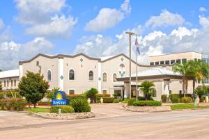 a large white building with a sign in front of it at Days Inn & Suites by Wyndham Webster NASA-ClearLake-Houston in Webster