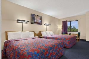 a hotel room with two beds and a chair and a window at Days Inn by Wyndham Buena Park in Buena Park