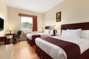 een hotelkamer met 2 bedden, een bureau en een raam bij Days Inn by Wyndham Chetwynd in Chetwynd