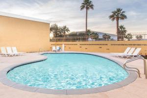 einen Pool in einem Hotel mit Stühlen und Palmen in der Unterkunft Days Inn by Wyndham Indio in Indio