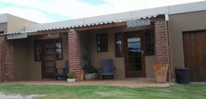 a brick house with a porch and two chairs at Rusthof Accommodation in Gansbaai
