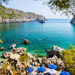 ein Strand mit blauen Sonnenschirmen und Menschen im Wasser in der Unterkunft Rea Hotel in Faliraki