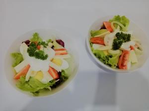 two bowls of vegetables and a salad on a white surface at Kutuh Manak Guest House in Uluwatu