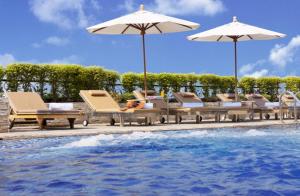 eine Gruppe von Stühlen und Sonnenschirmen neben einem Pool in der Unterkunft Intimate Hotel Pattaya - SHA Extra Plus in Pattaya