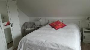 a white bed with a red pillow and a chair at Haus Nautilus in Helgoland