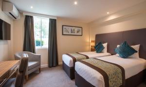 Habitación de hotel con 2 camas y escritorio en Thistle London Heathrow Terminal 5 en Hillingdon