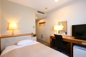 a hotel room with a bed and a desk with a television at Sentia Hotel Naito in Kofu