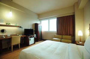 a hotel room with a bed and a desk and a television at Kindness Hotel Wu-Jia in Kaohsiung