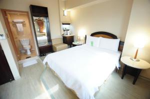 a bedroom with a large white bed and a toilet at Kindness Hotel Weiwuying in Kaohsiung