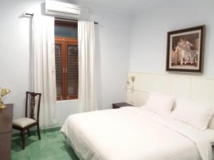 a white bedroom with a bed and a chair at Griya Asih in Yogyakarta