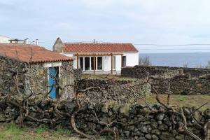a house behind a stone wall with the ocean in the background at Canário do Mar - Rural Tourism in Angra do Heroísmo