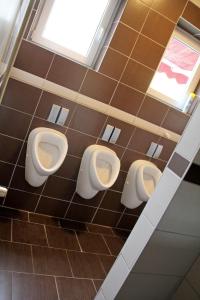 a bathroom with three urinals on a tiled wall at Pension Kupferkanne in Dingolfing