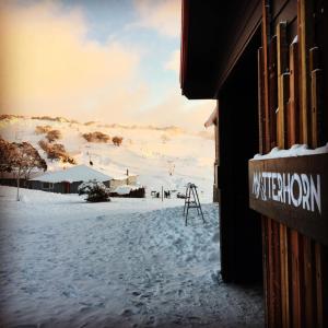 a snow covered field with a building and a sign at Matterhorn Lodge in Perisher Valley