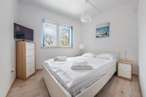 1 dormitorio con 1 cama con sábanas blancas y TV en Apartamenty Sun & Snow Zwycięstwa, en Międzyzdroje