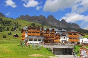 a large building on a hill with mountains in the background at Hotel San Marco in Passo San Pellegrino