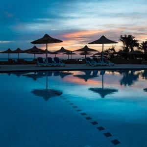 a swimming pool with chairs and umbrellas at sunset at Silver Beach Boutique Hotel in Quseir