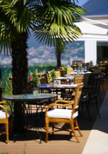 eine Terrasse mit Tischen, Stühlen und einer Palme in der Unterkunft Suitenhotel Parco Paradiso in Lugano