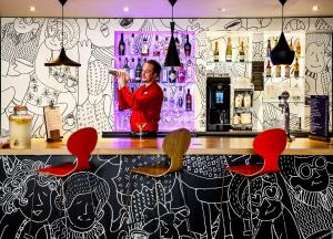 a man standing behind a bar with red chairs at ibis London Greenwich in London