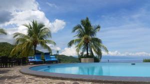 a swimming pool with palm trees and chairs on a beach at Infinity Heights Resort in Siquijor