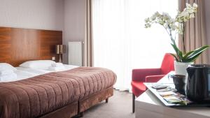 um quarto de hotel com uma cama e uma cadeira vermelha em Bazuny Hotel&Spa em Kościerzyna
